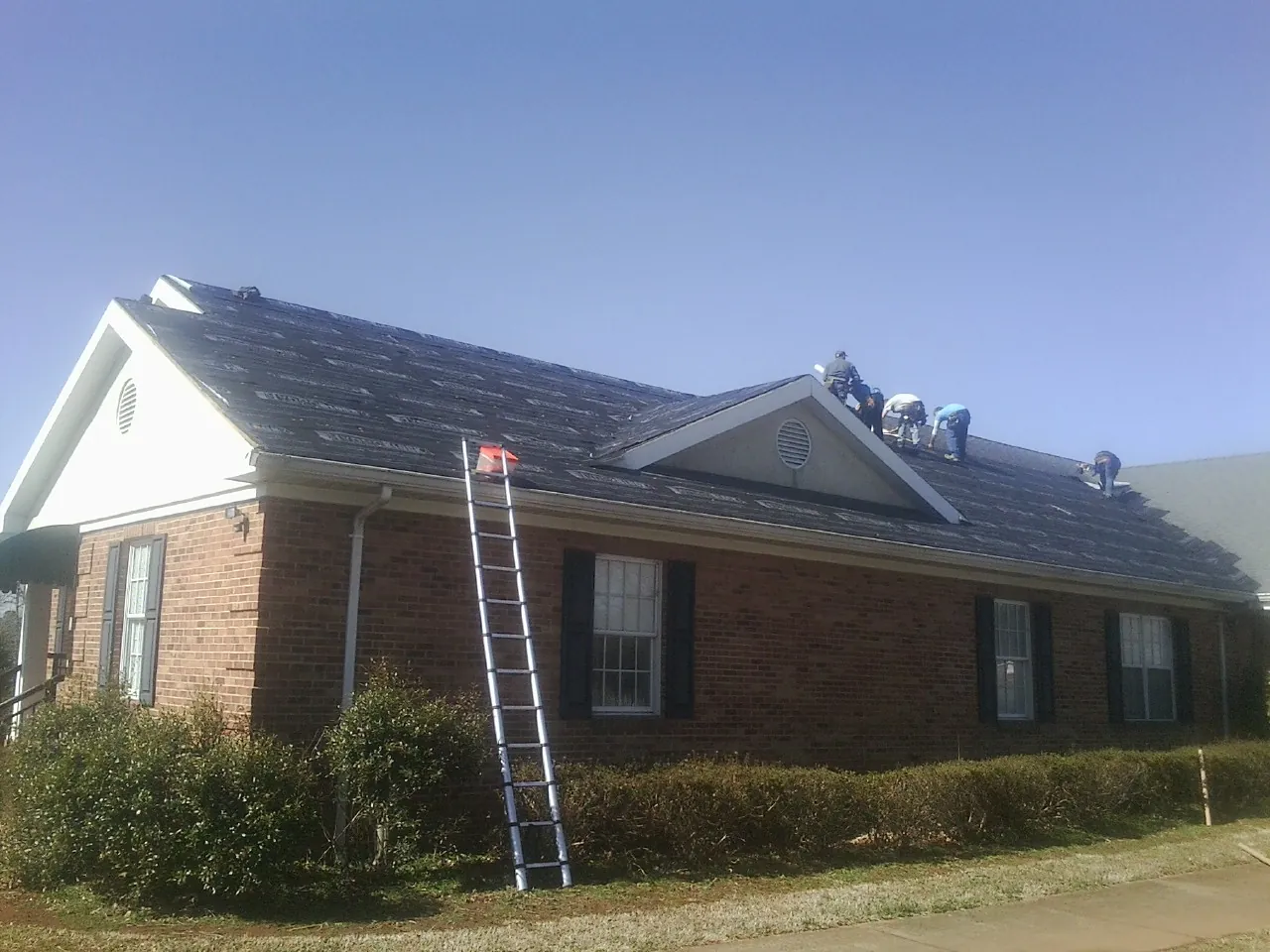 Crew tearing shingles off a brick ranch roof with a ladder set — Metal Roof Repair work by our crew in Staplehurst
