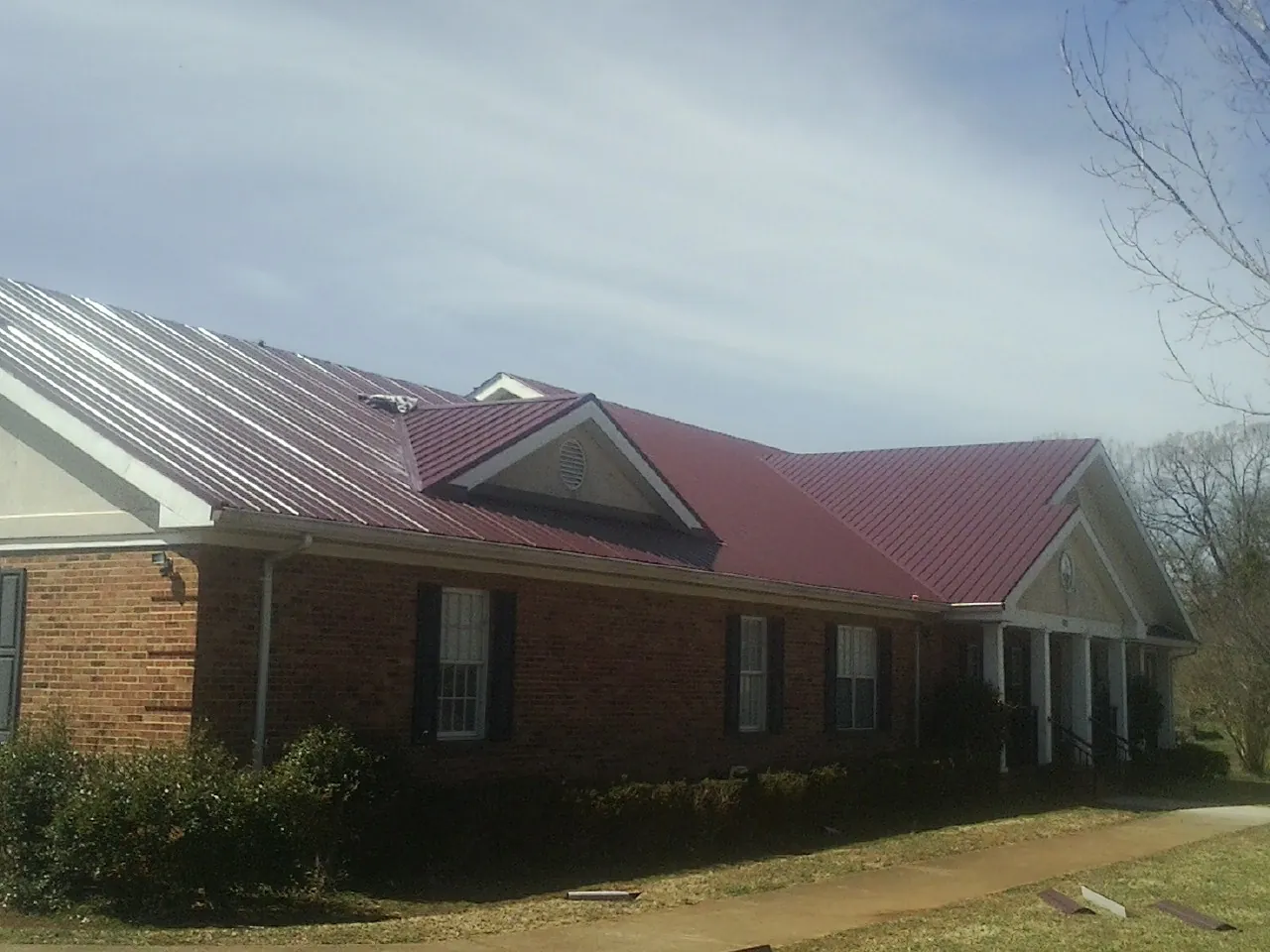 Red metal roof with gabled entries on a long brick building, from a Hail Damage Roof Repair job in Staplehurst