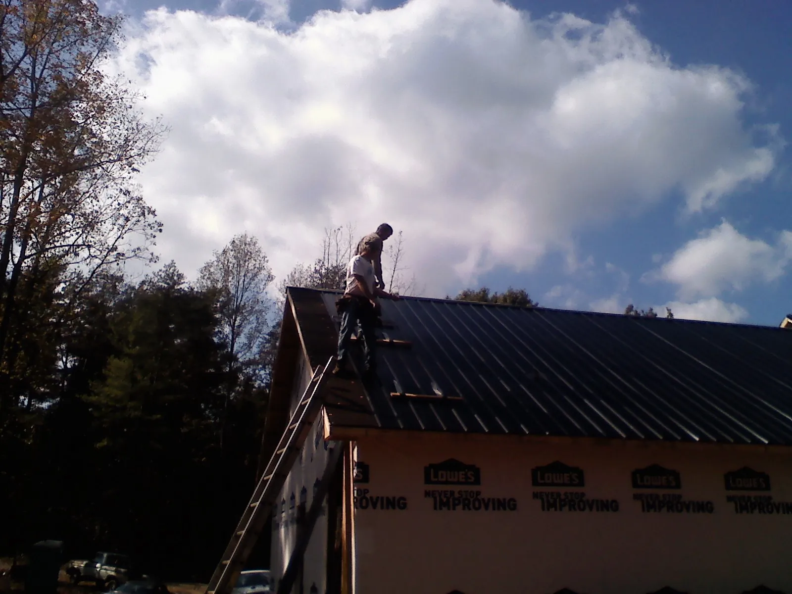 Roofer fastening dark metal panels high against a cloudy sky, from a Roof Inspection job in Staplehurst