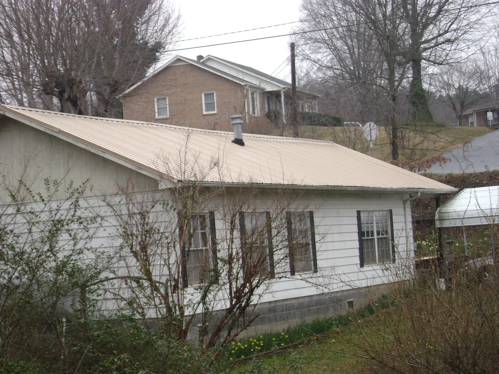 Tan metal roof on a white sided house set into a hillside — Commercial Roofing by Roofing Brothers in Staplehurst